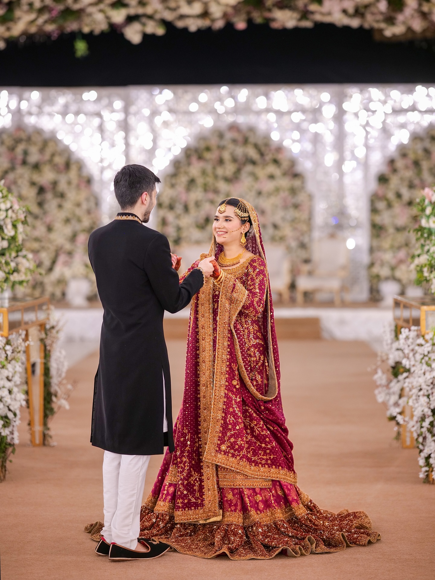 Bride and groom holding hands on a flower-lined aisle beneath a floral arch